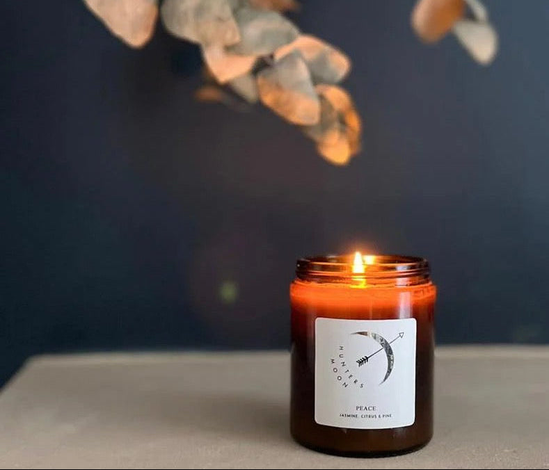 Candle in a glass jar with a label on a surface, with a dark background and decorative elements.